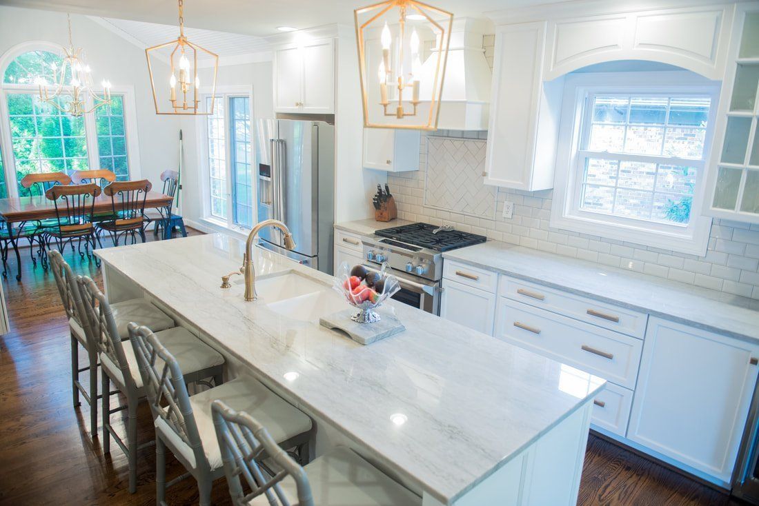 Bright white kitchen with marble island, pendant lights, and dining table by large windows