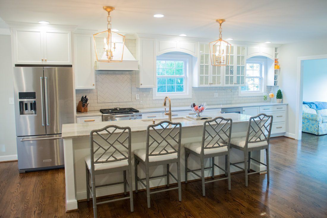Bright modern kitchen with stainless steel fridge, white cabinets, island seating, and hardwood floors