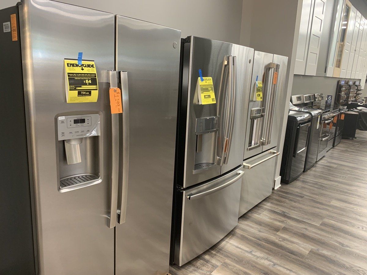 Row of stainless steel kitchen refrigerators with water dispensers in a store showroom.