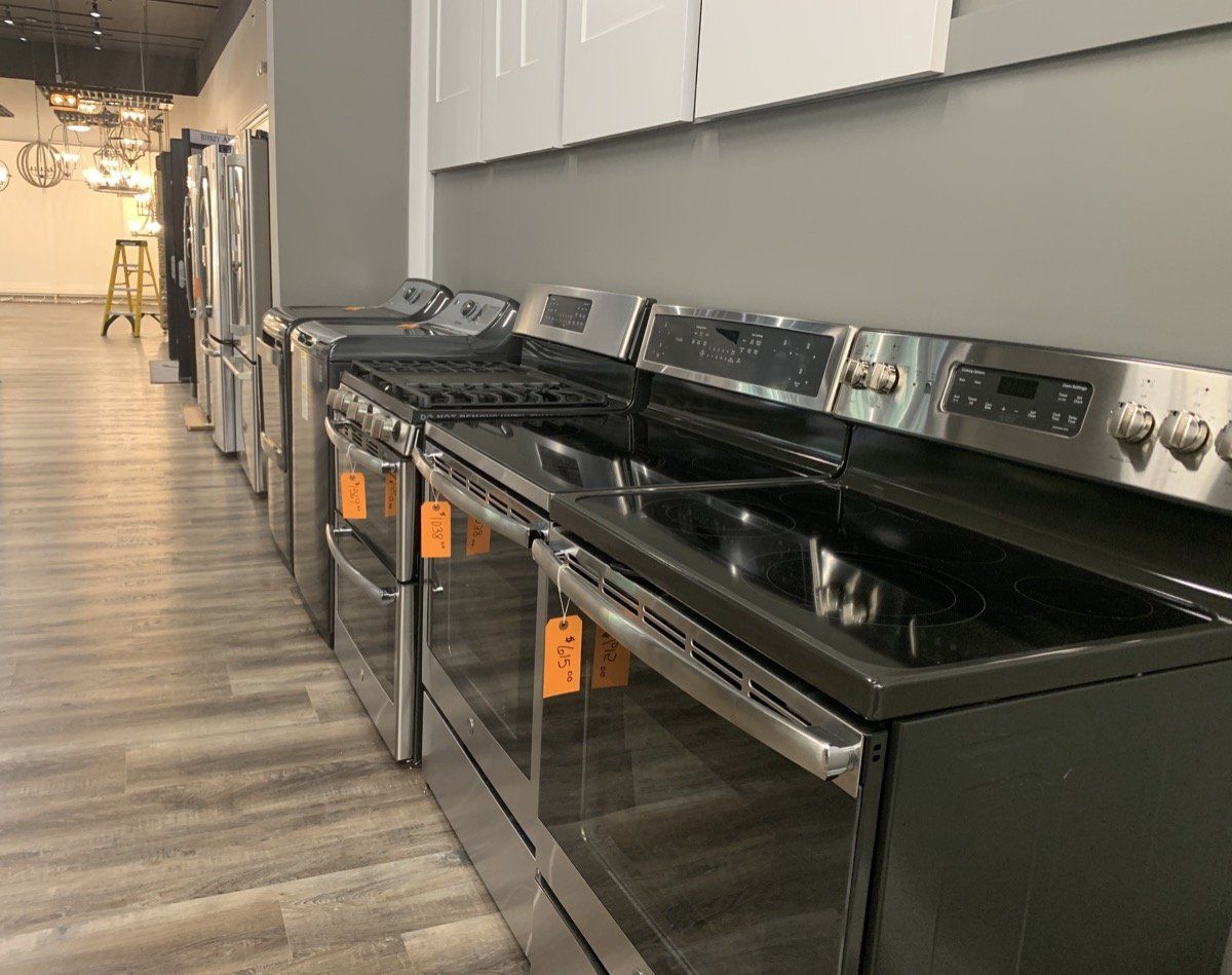 A row of black stainless steel stoves in a showroom aisle with wood-look flooring