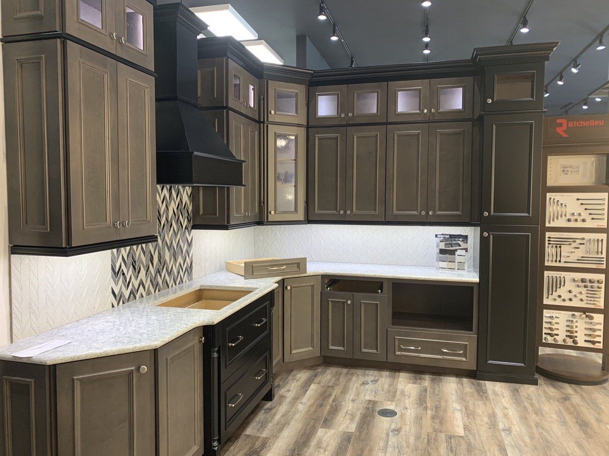 Modern kitchen showroom with dark wood cabinets, white countertops, and patterned backsplash.