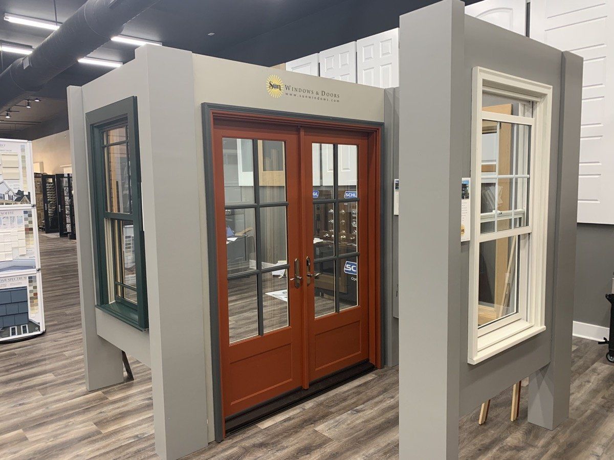 Display of two exterior doors: a dark wood double door and a white windowed door in a showroom.