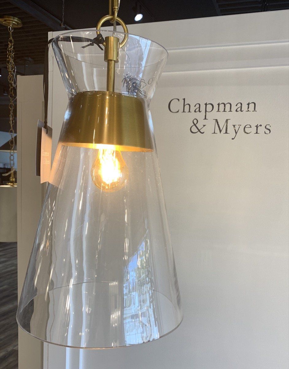 Glass pendant light with brass accents in front of a Chapman & Myers sign
