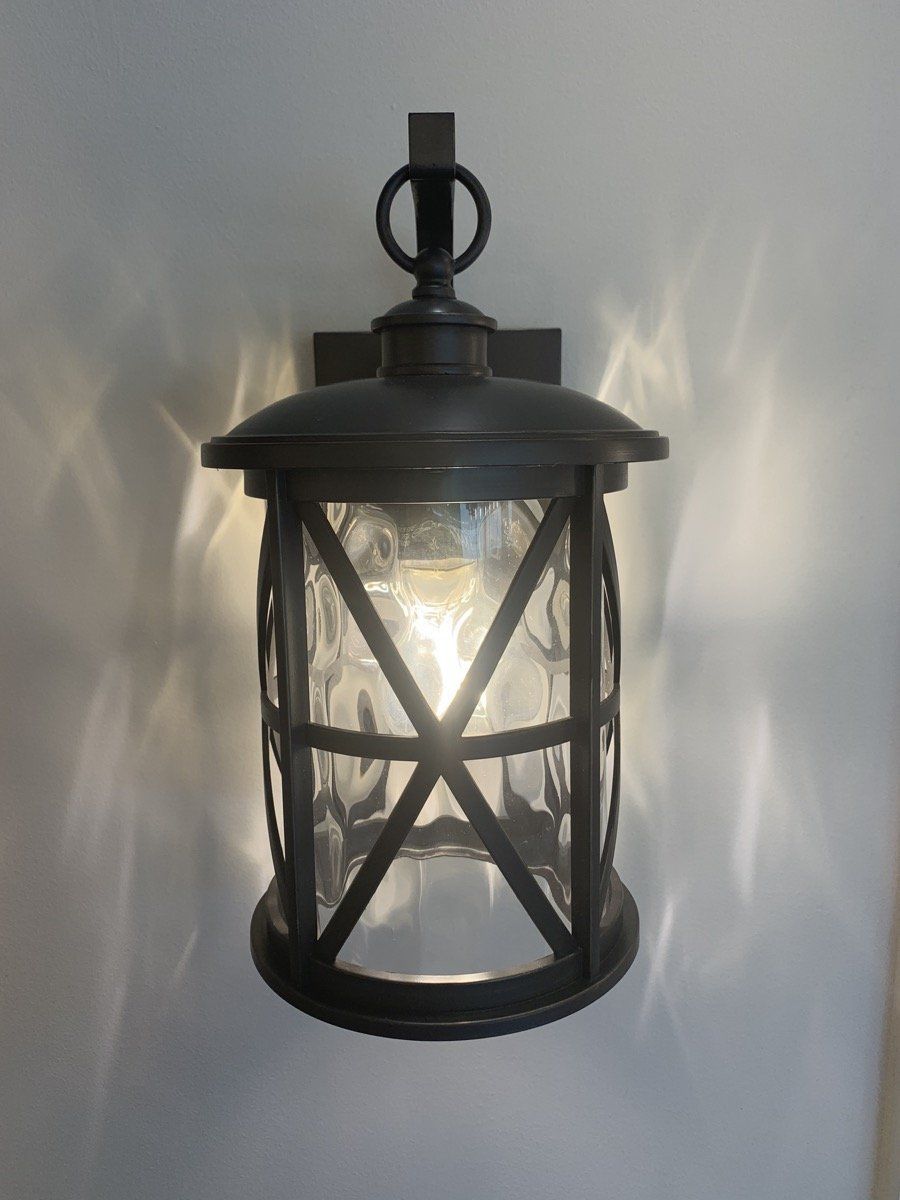 Black metal outdoor lantern on a wall, lit from within, casting patterned light.