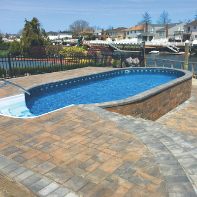 Backyard pool with brick patio beside a waterfront neighborhood on a sunny day