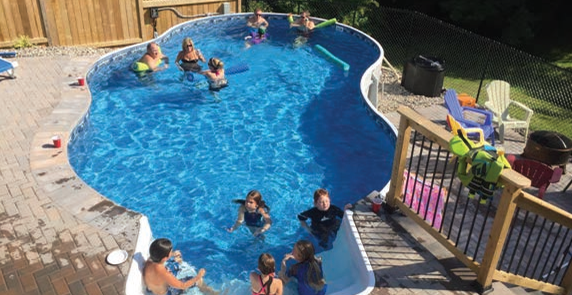People swimming in a blue backyard pool with a deck and railing nearby