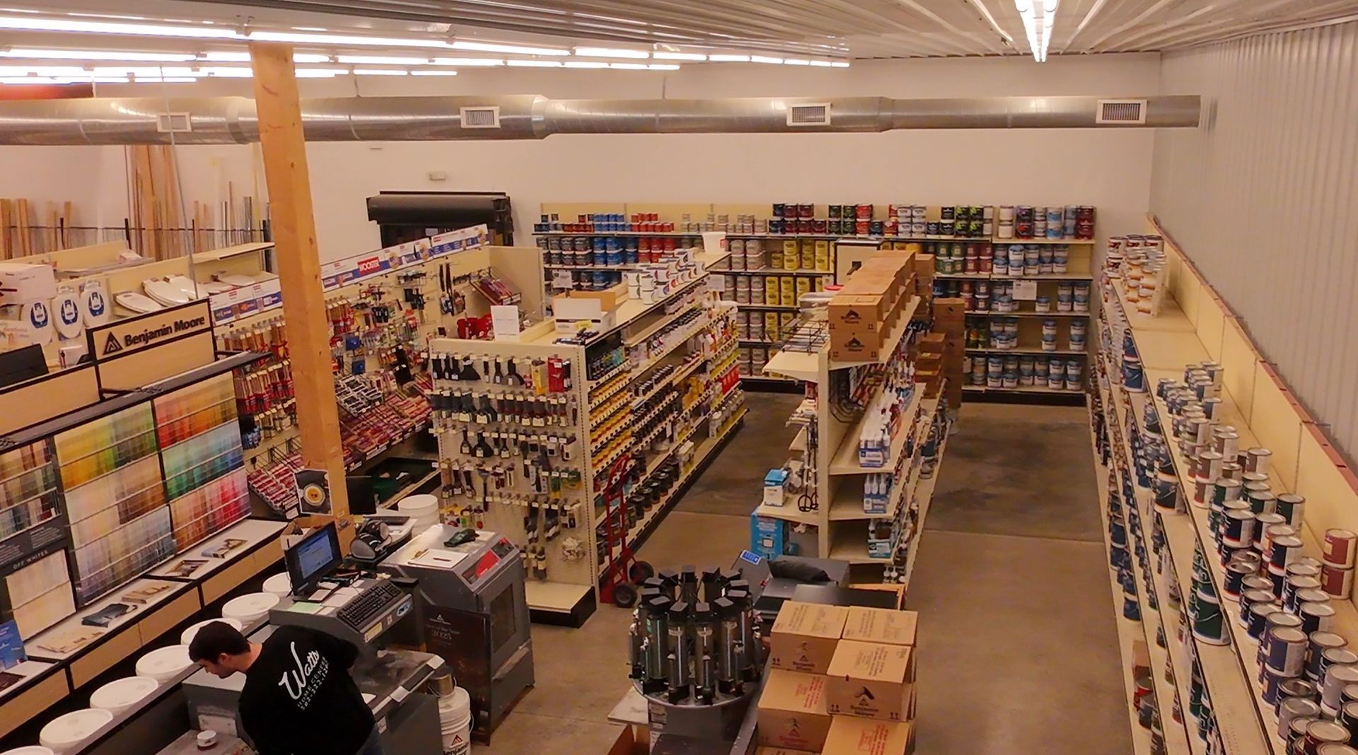 Wide view of a small grocery store aisle with shelves of packaged goods and a checkout counter.