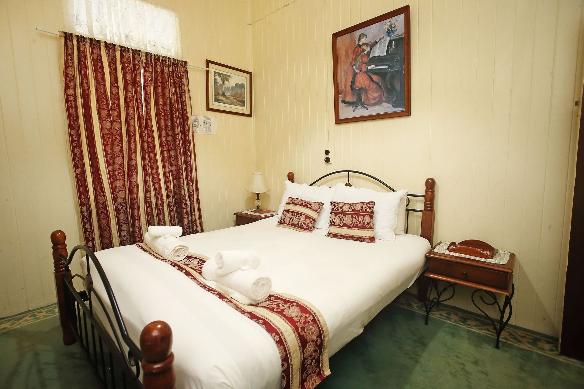 Bedroom with double bed, red patterned curtains, art, and bedside tables.