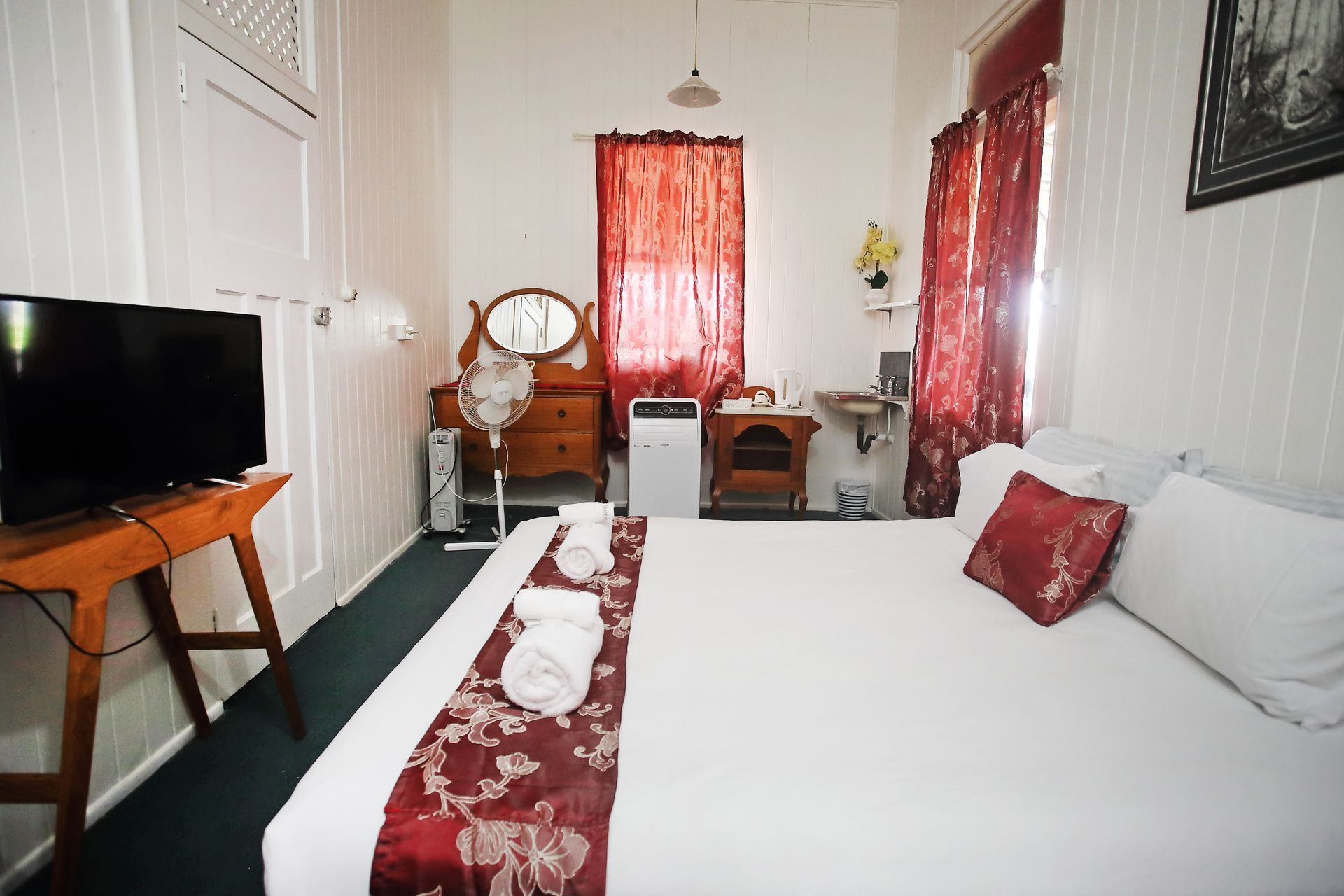 Bedroom with bed, TV, dresser, and red curtains.