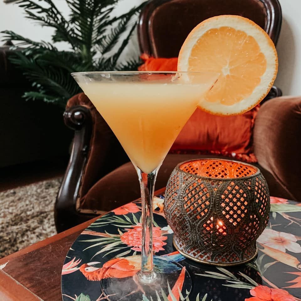 Cocktail in a martini glass with orange slice, next to a lit candle.