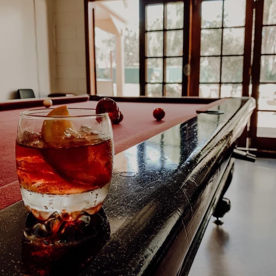 Cocktail on pool table with red felt; outdoor view through open doors.
