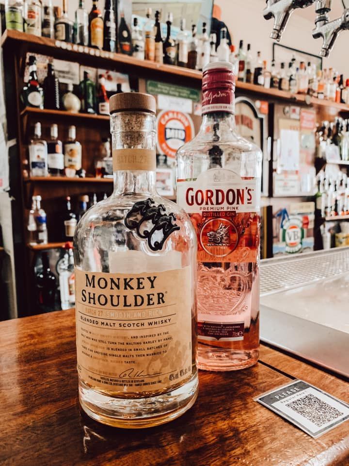Two liquor bottles, Monkey Shoulder whiskey and Gordon's pink gin, on a bar top in a bar.