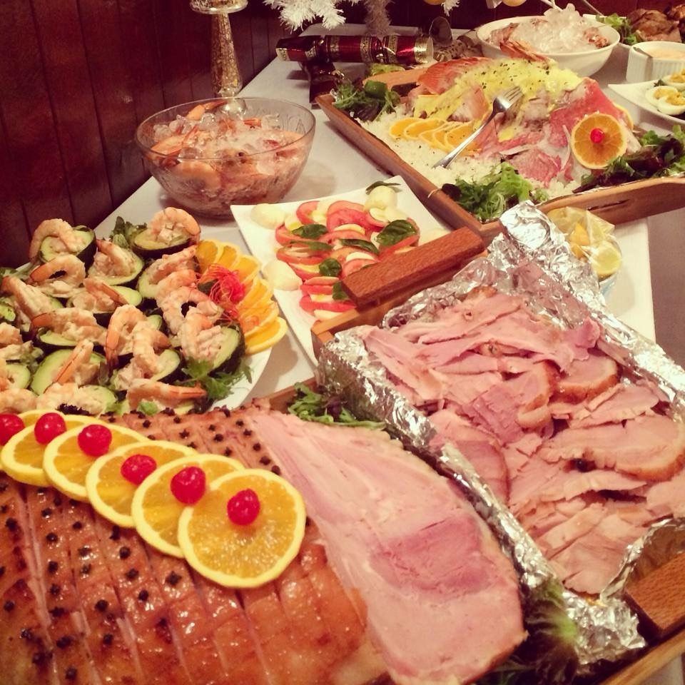 Buffet table with ham, shrimp, salads, and garnishes, with orange and cherry decorations.