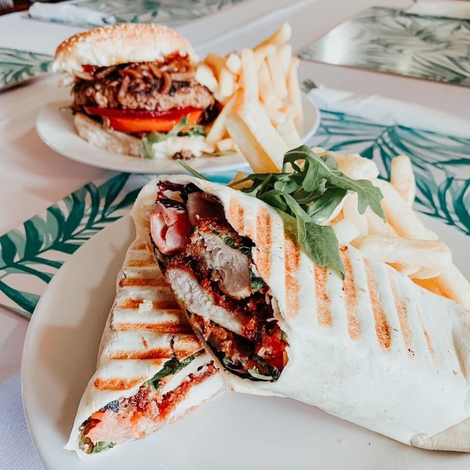 Burger and wrap with fries on plates, on a table with leaf-patterned tablecloth.