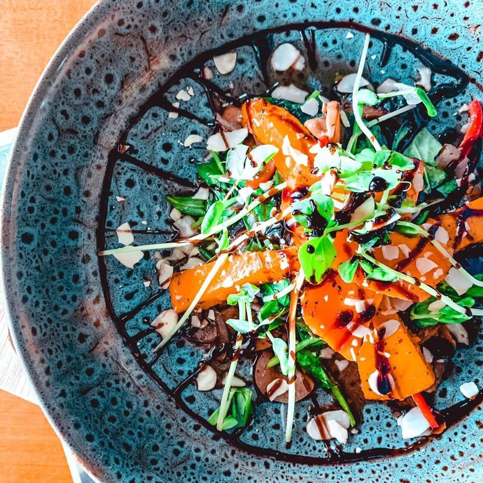 Roasted vegetable salad with balsamic glaze, almonds, and microgreens in a blue bowl.