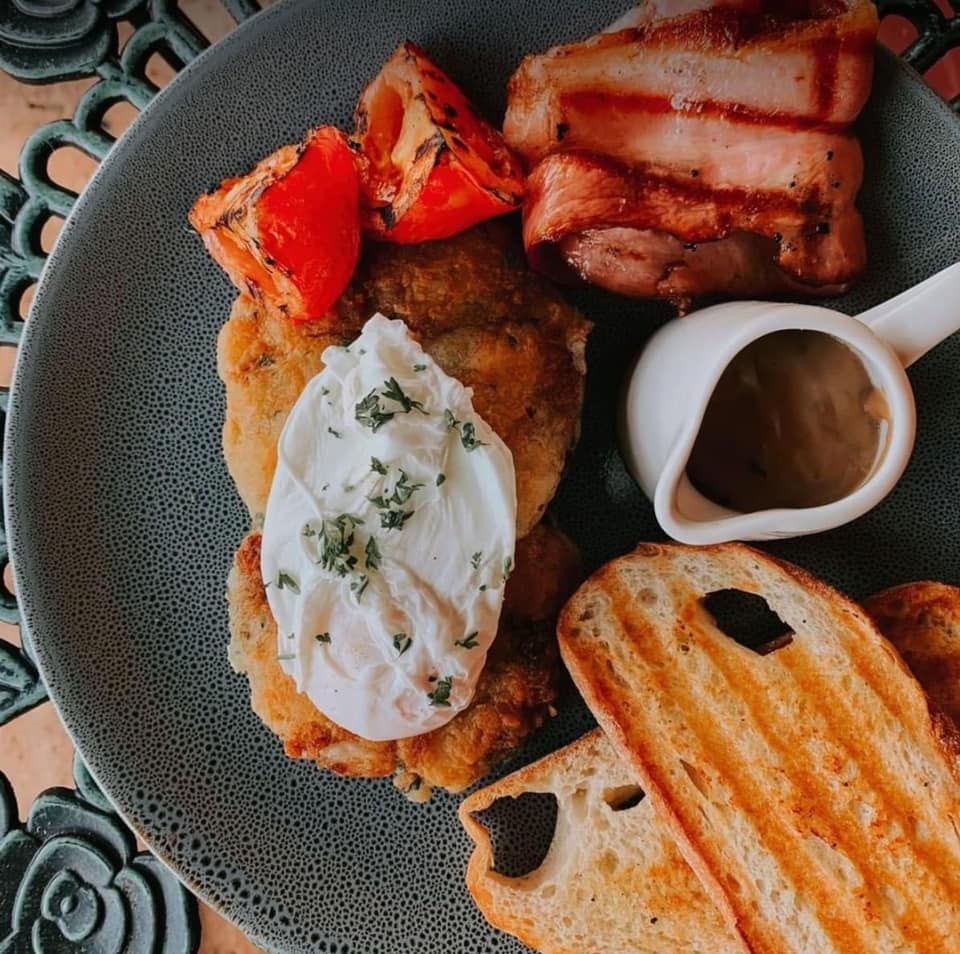 Breakfast plate with potato cakes, poached egg, bacon, tomatoes, toast, and gravy.