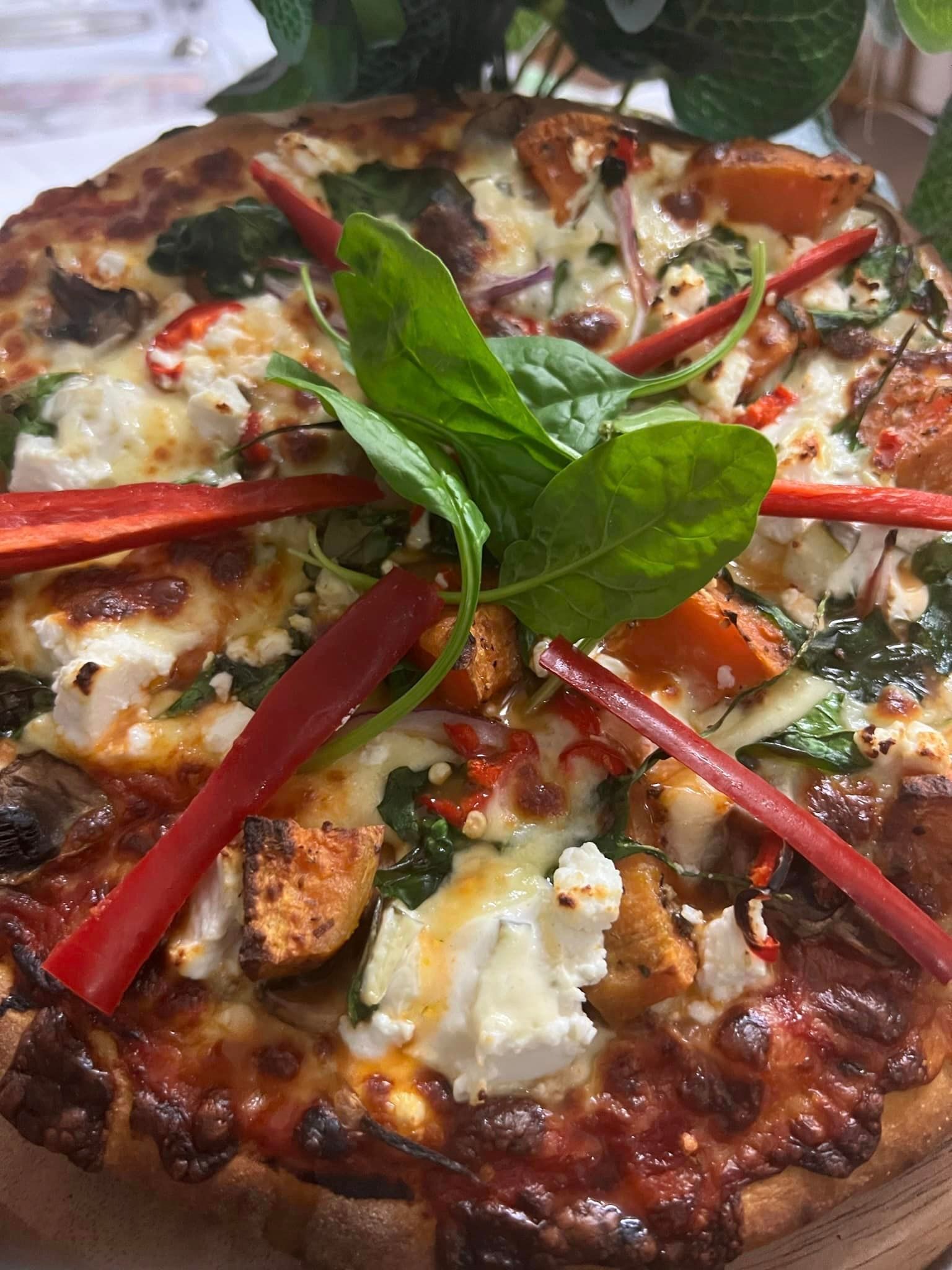 Pizza topped with cheese, spinach, red peppers, and greens.