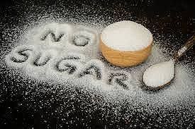 The word no sugar is written in powdered sugar next to a bowl of sugar and a spoon.