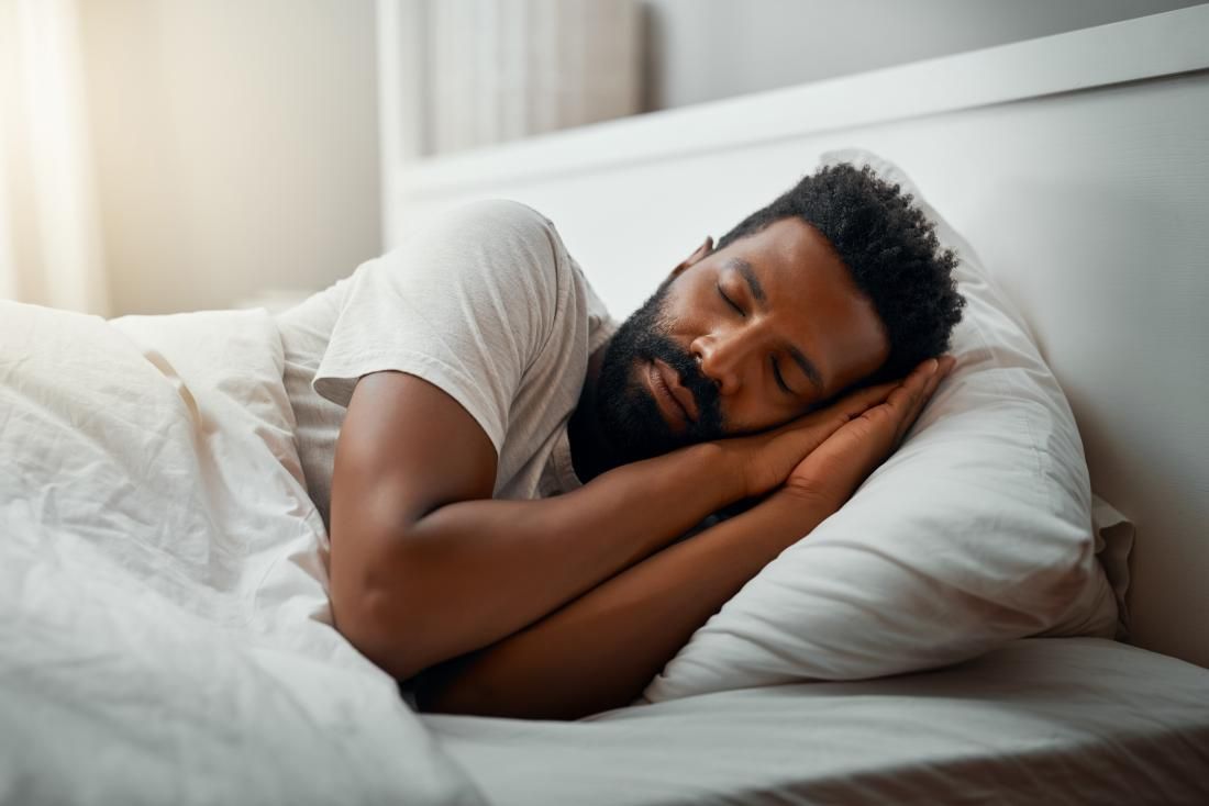 A man with a beard is sleeping in a bed with white sheets and pillows.