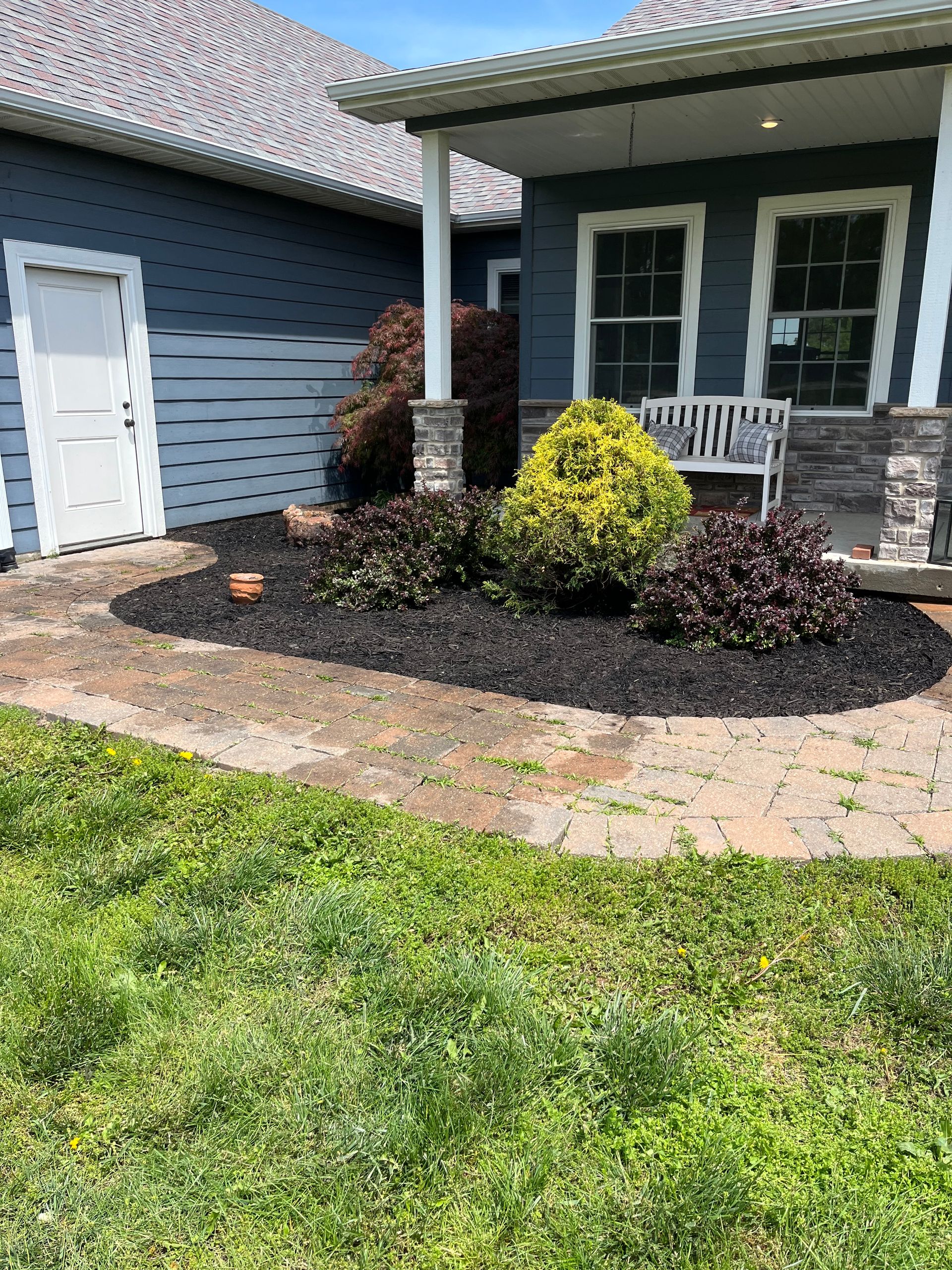 Front yard landscaping with mulch bed, shrubs, and a house porch beside a garage