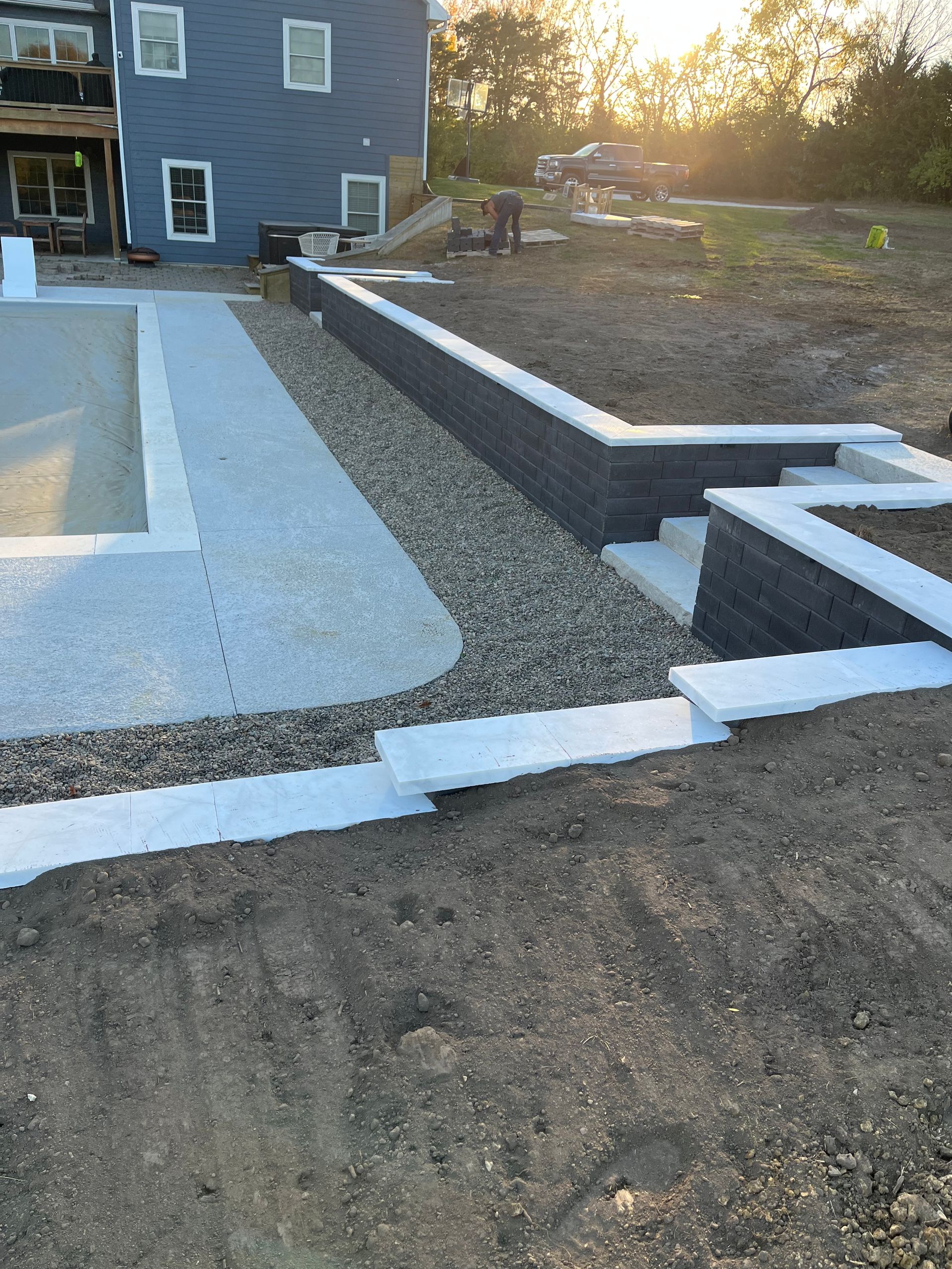 New concrete walkway and retaining wall beside a gray house at sunset