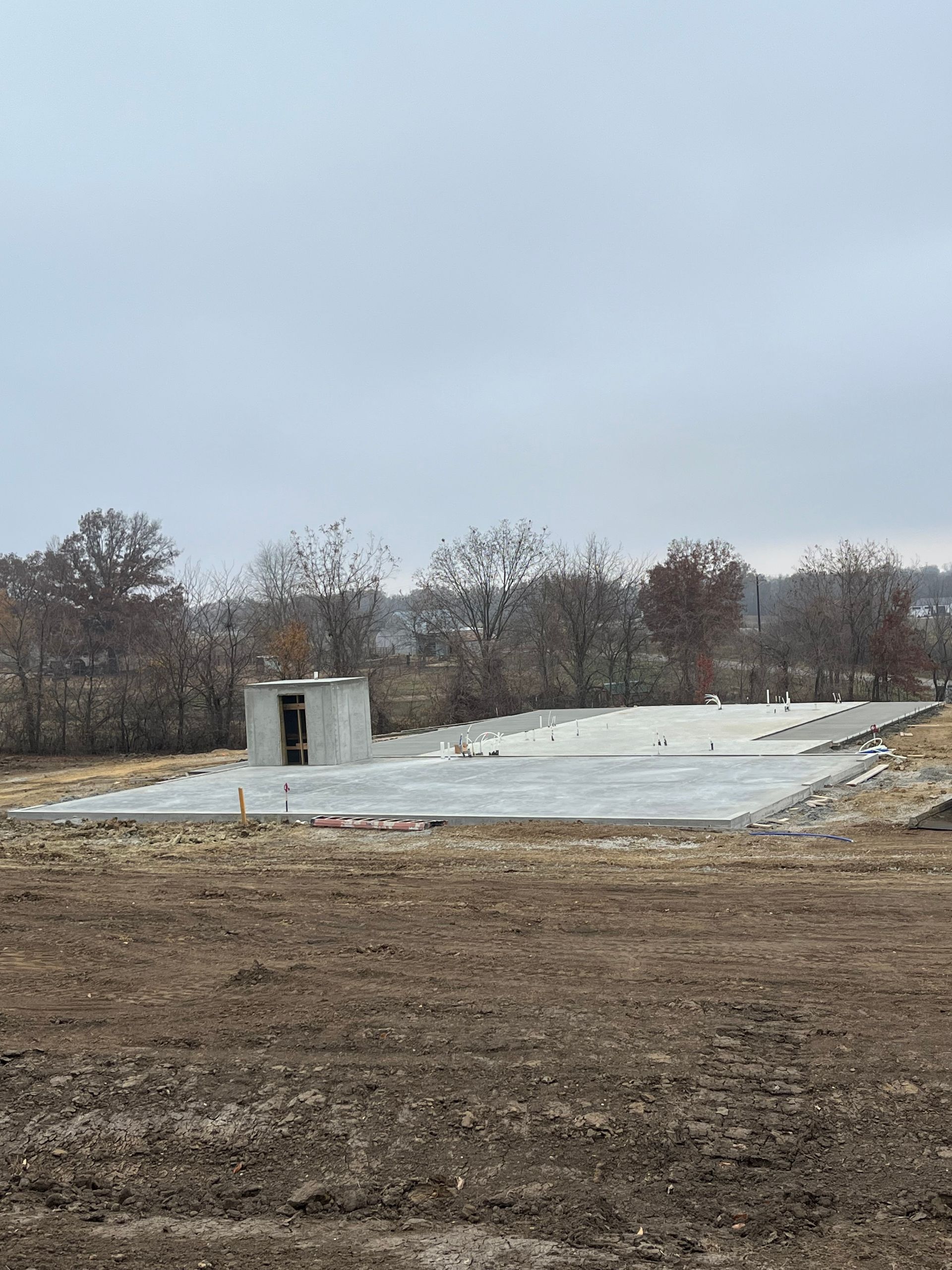 Concrete foundation slab at a construction site with a small block structure and bare trees in the background