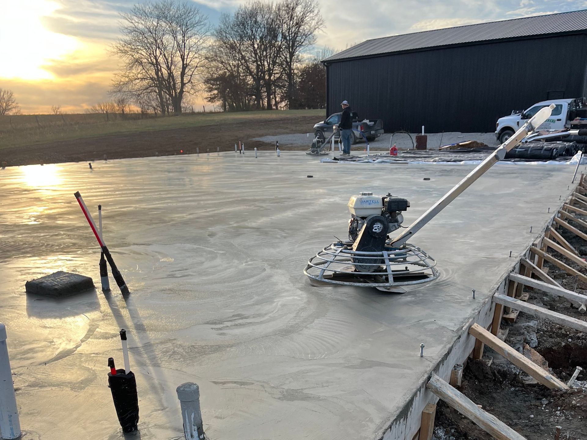Concrete slab being smoothed with power trowels at sunset on a construction site