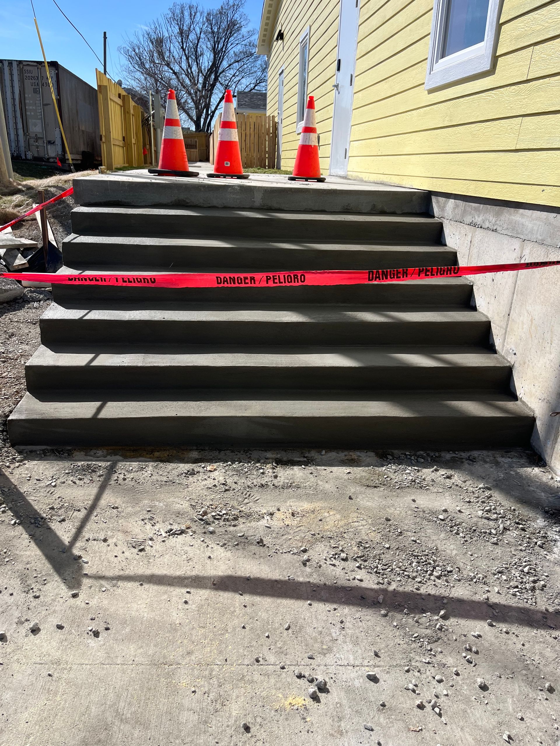 Concrete stairs blocked by red caution tape and orange traffic cones outside a yellow building