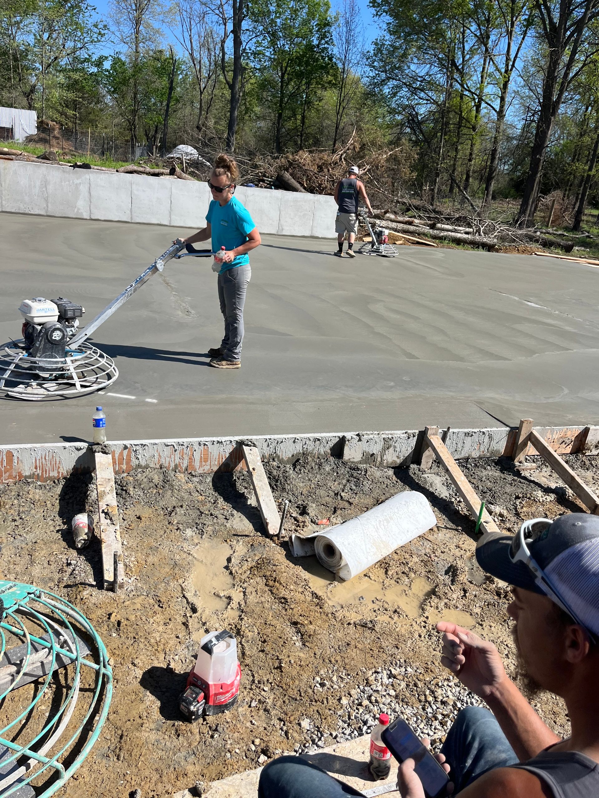 Worker smoothing fresh concrete with a power trowel at a construction site, another worker in background