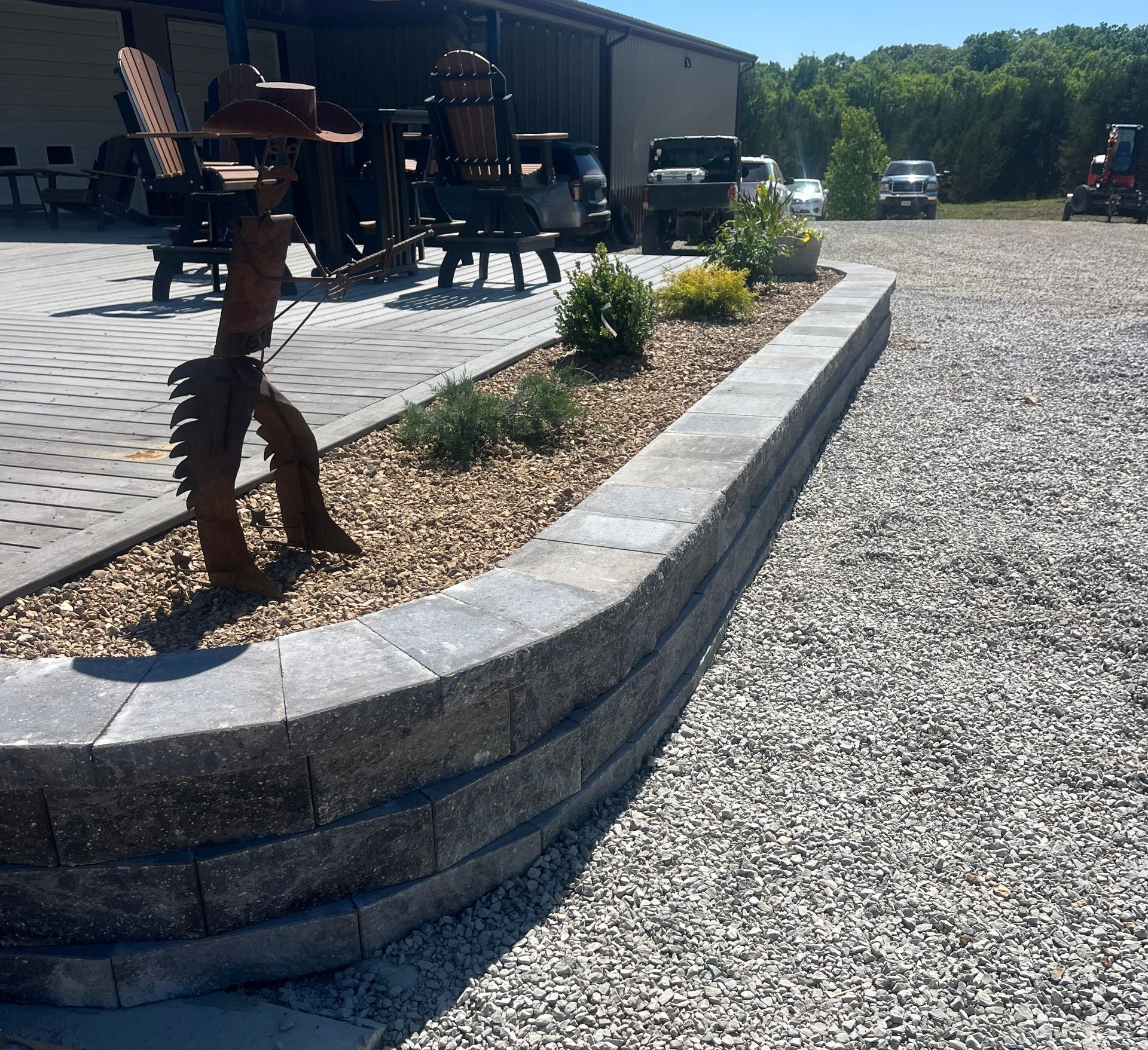 Landscaped gravel lot with raised stone planter and patio chairs beside a building