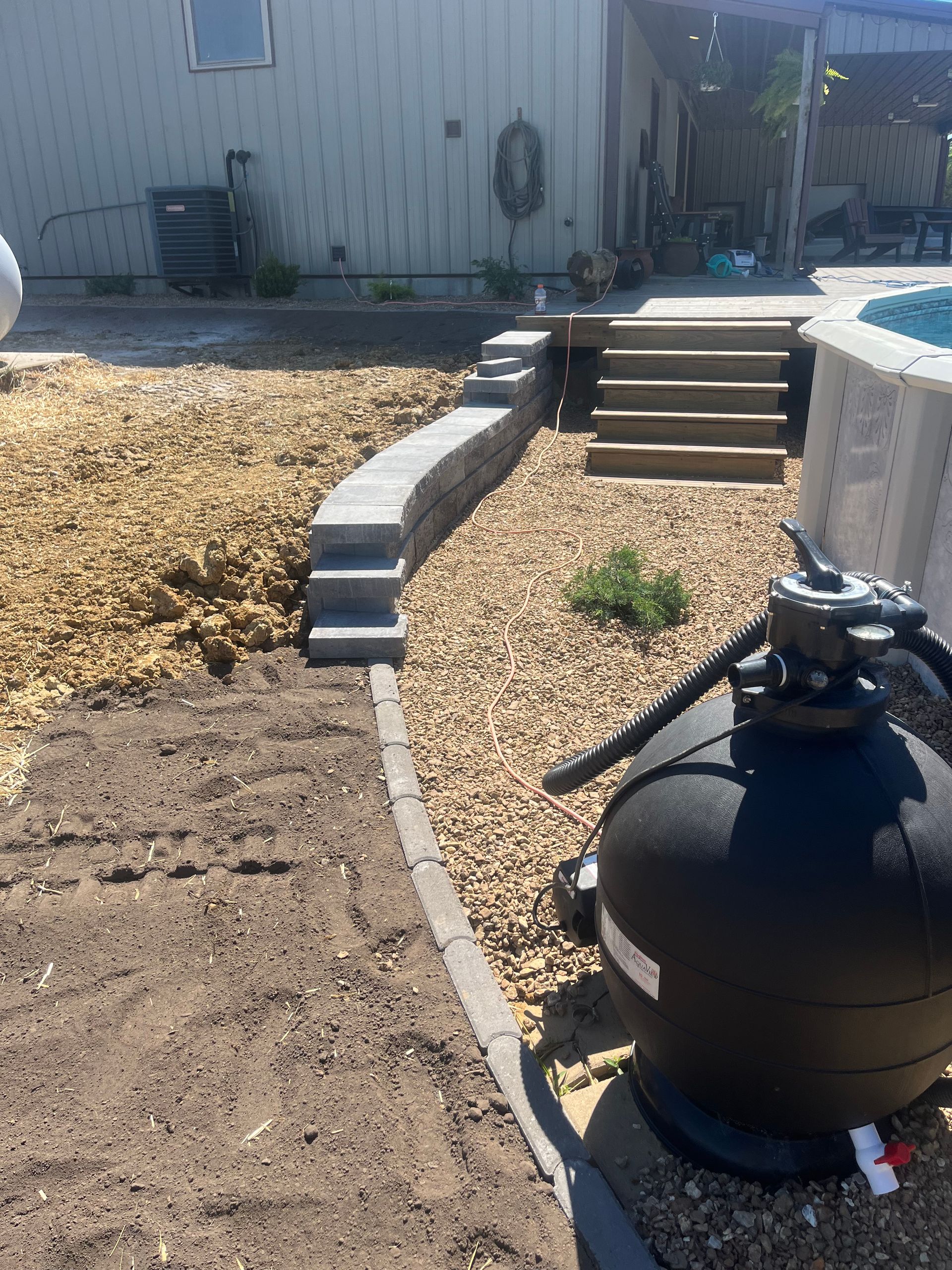 Backyard patio with steps, gravel, retaining wall, and a black fire pit in the foreground