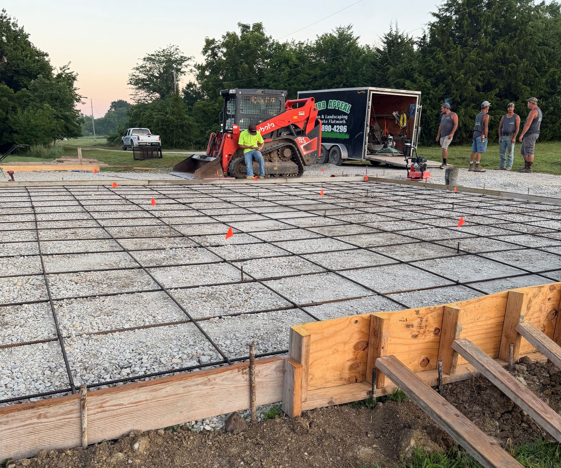 Construction crew pouring concrete foundation slab with orange excavator on site at dusk