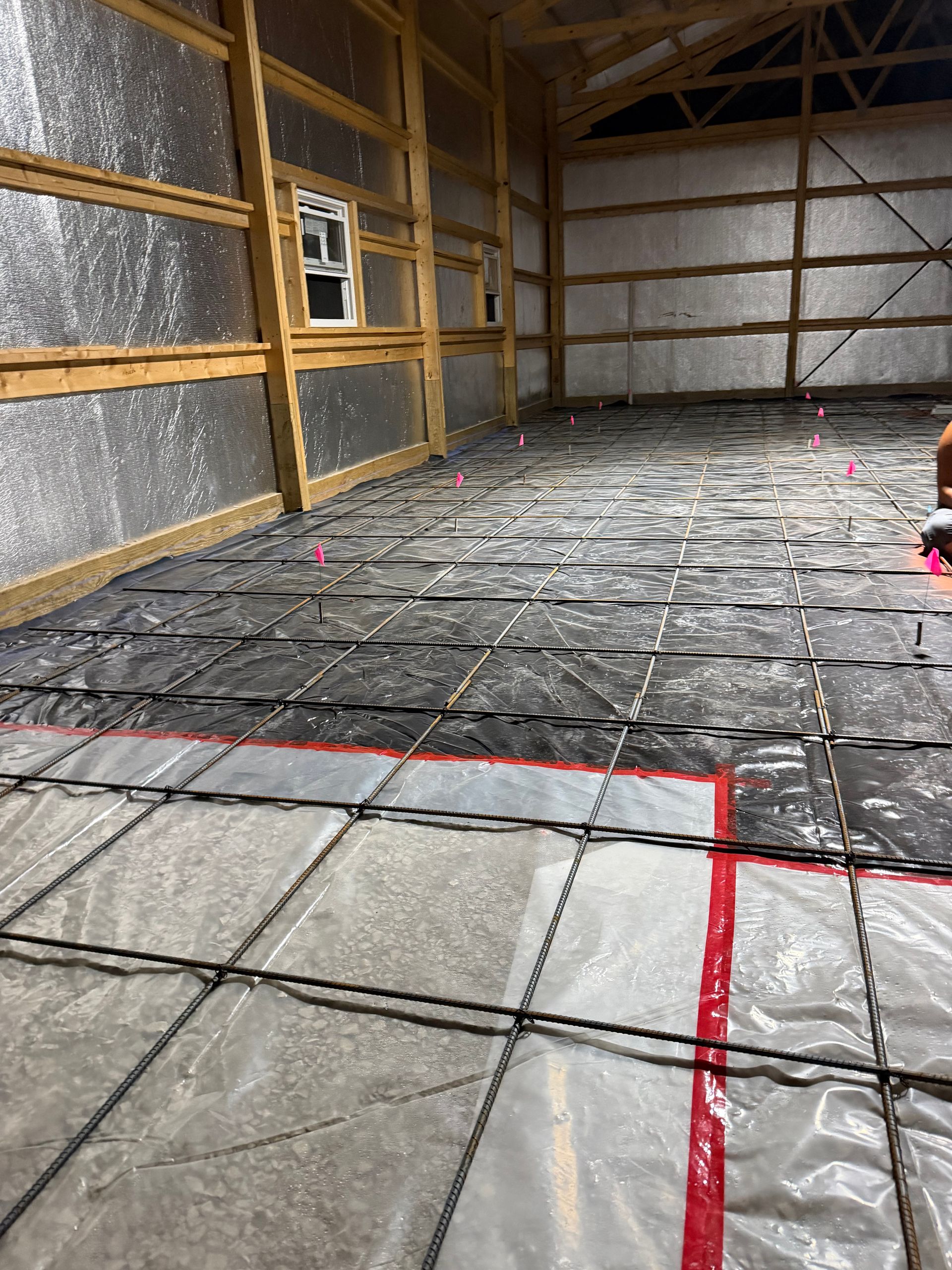 Unfinished warehouse interior with insulated walls and a black plastic-covered floor marked by red tape lines.