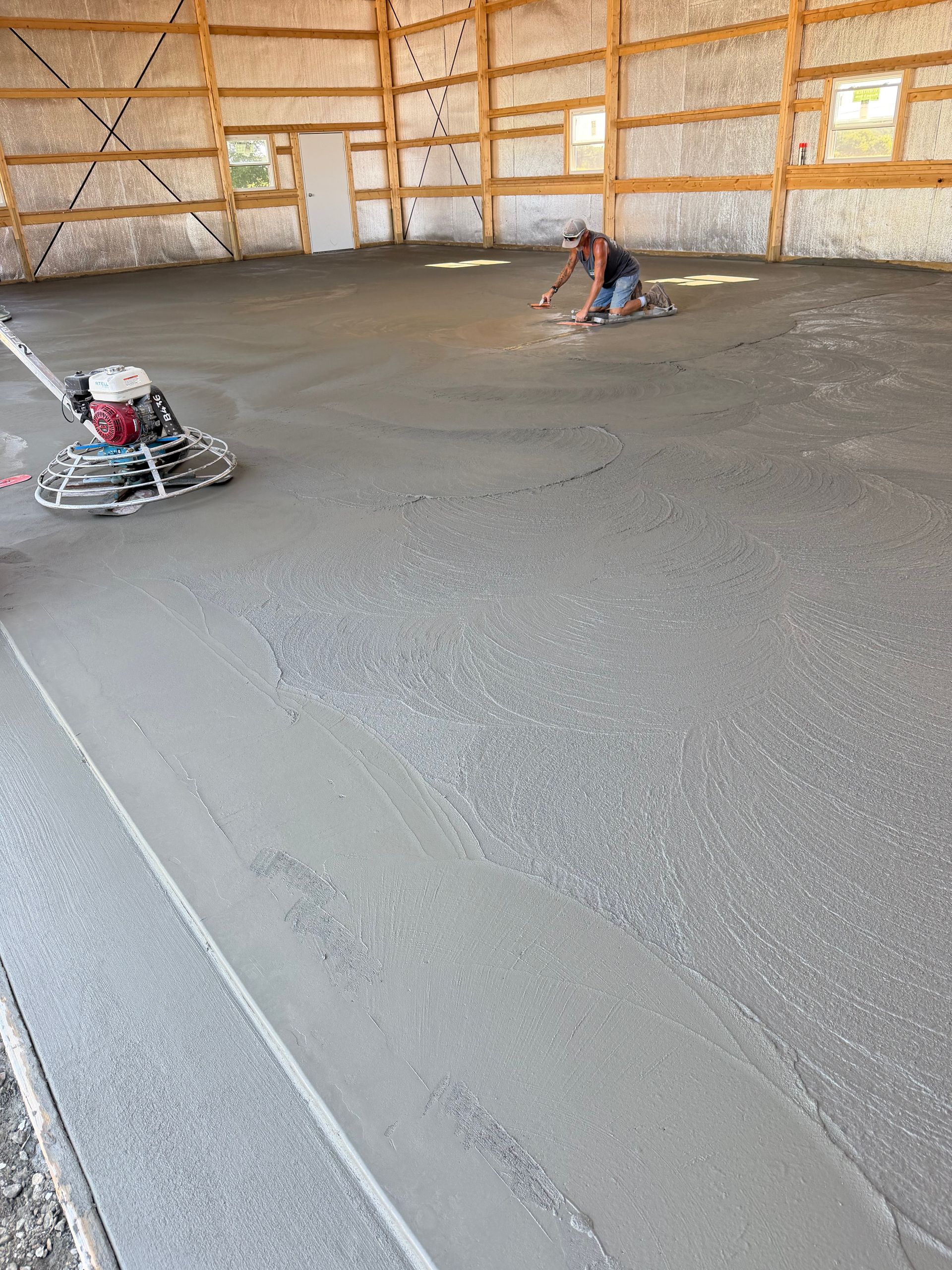 Workers smoothing a fresh concrete floor inside an unfinished wooden building