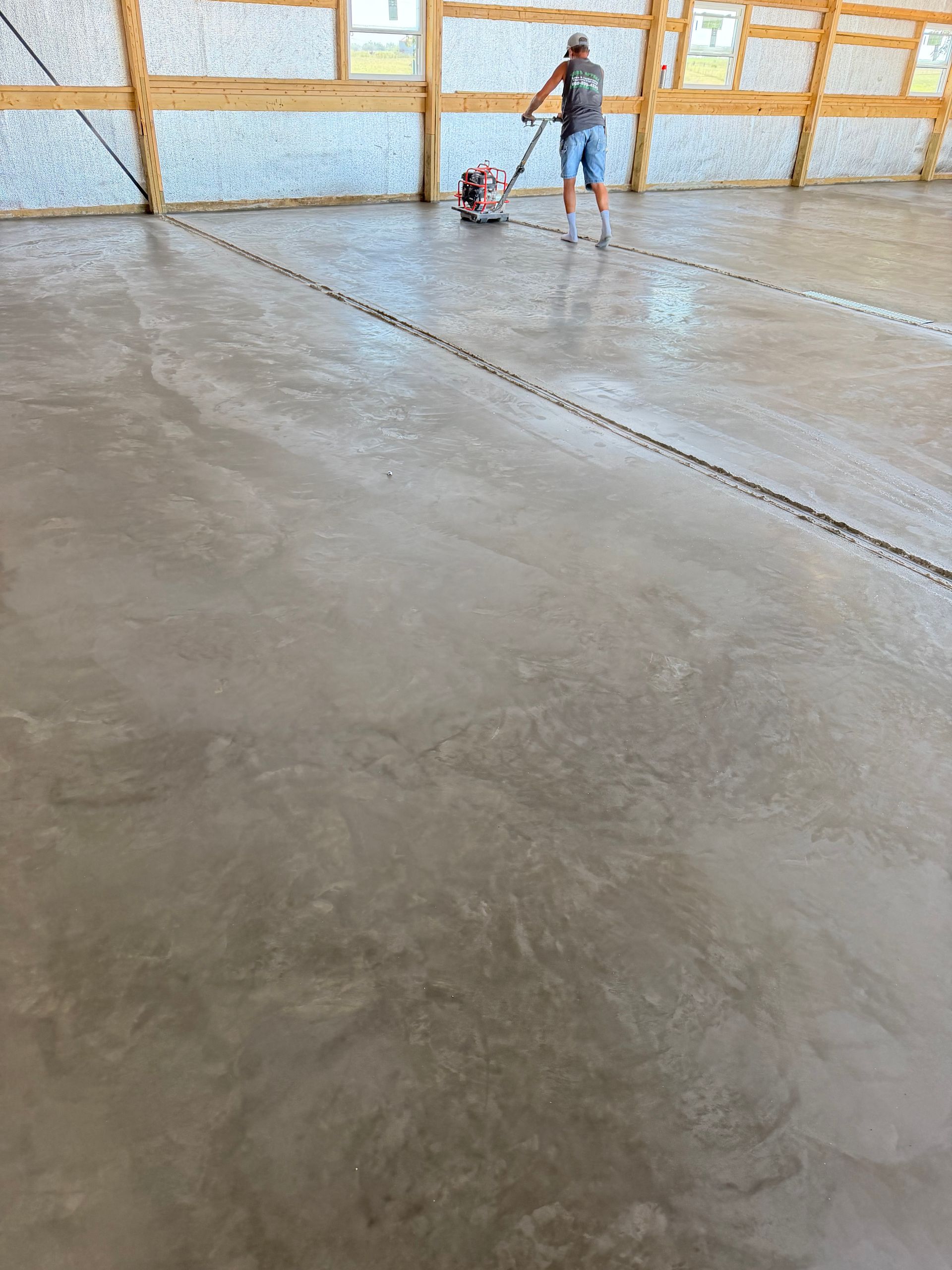 Worker and child in a large concrete-floored room with wooden framing and a water view beyond the wall.