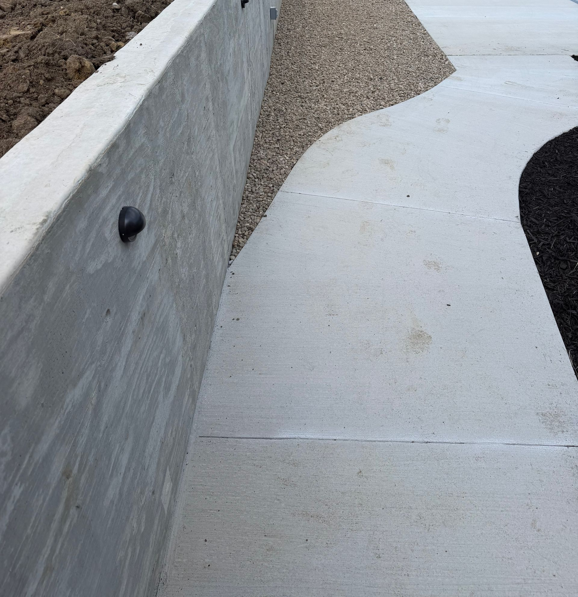 Concrete retaining wall with a gravel pile spilling onto a light gray walkway