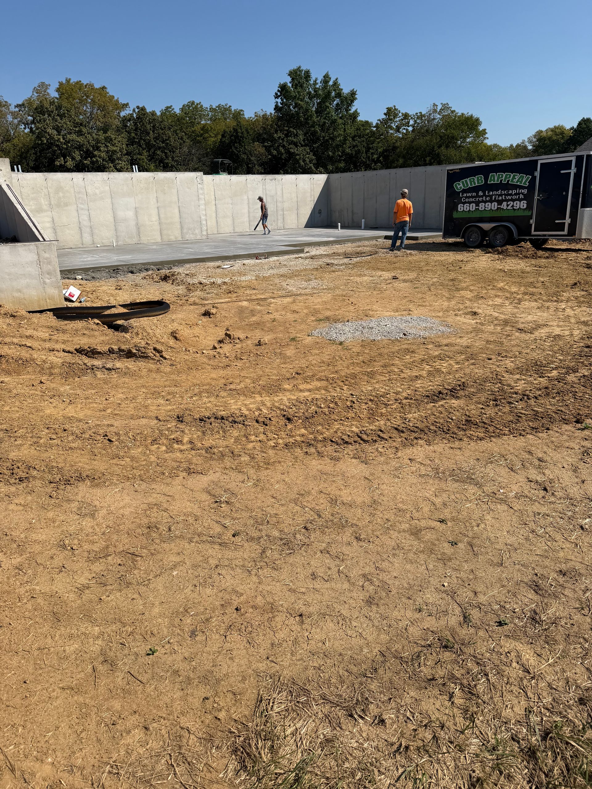 Construction site with a concrete wall, dirt lot, and worker near a dumpster under a clear sky