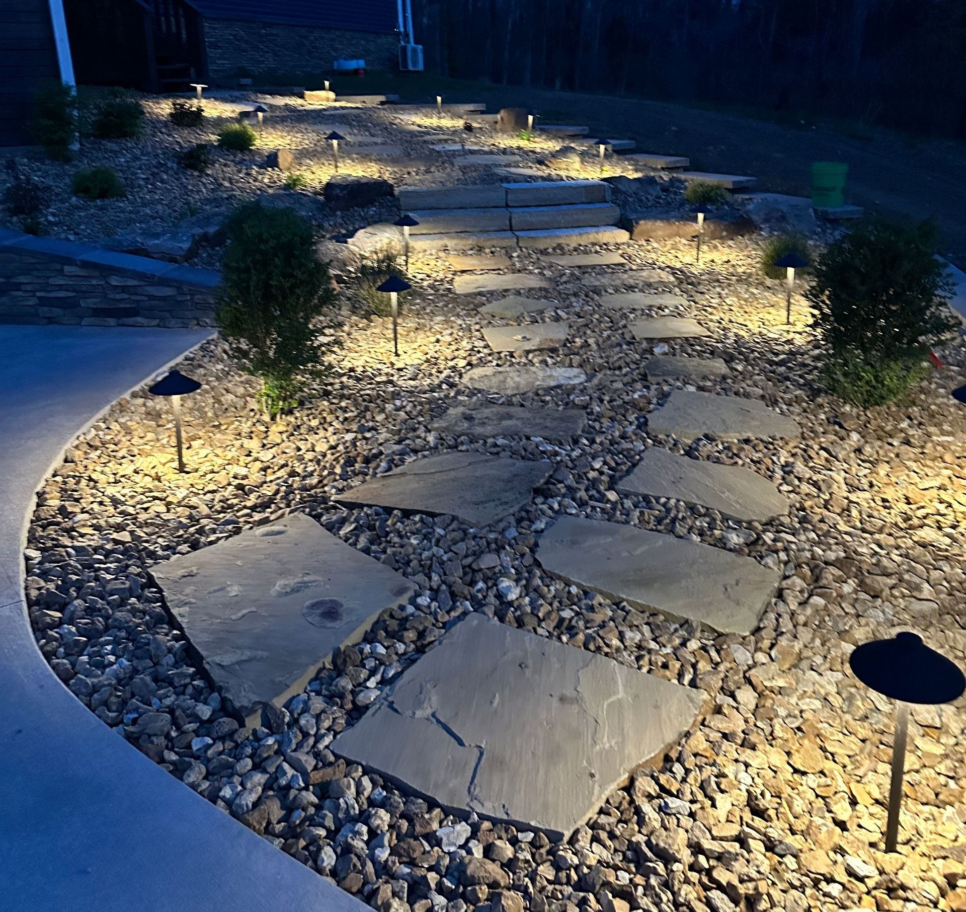 Curved stone path with soft ground lights and small shrubs in a landscaped garden at night