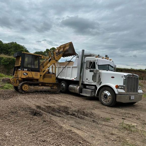 White dump truck being loaded by a yellow excavator on a gravel lot under cloudy skies