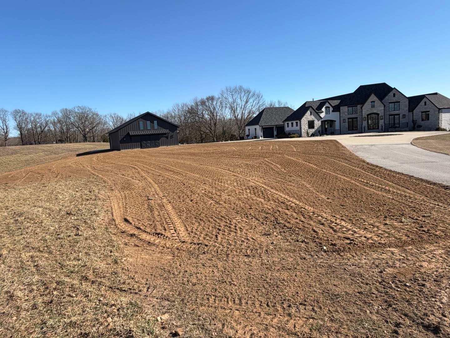 Gravel lot beside a new suburban home, with a curved driveway and bare trees under a clear blue sky
