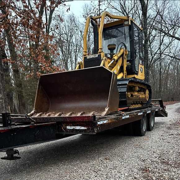 Yellow bulldozer on a flatbed trailer in a wooded outdoor area