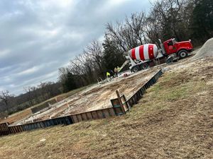 Red-and-white cement mixer truck on a rural roadside beside a concrete slab under cloudy skies