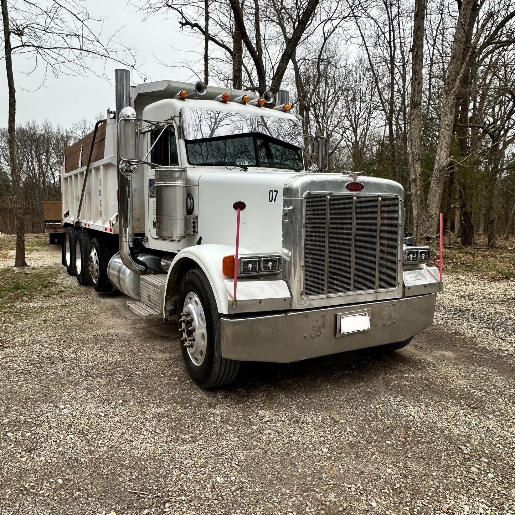 White dump truck parked on a gravel road amid bare trees