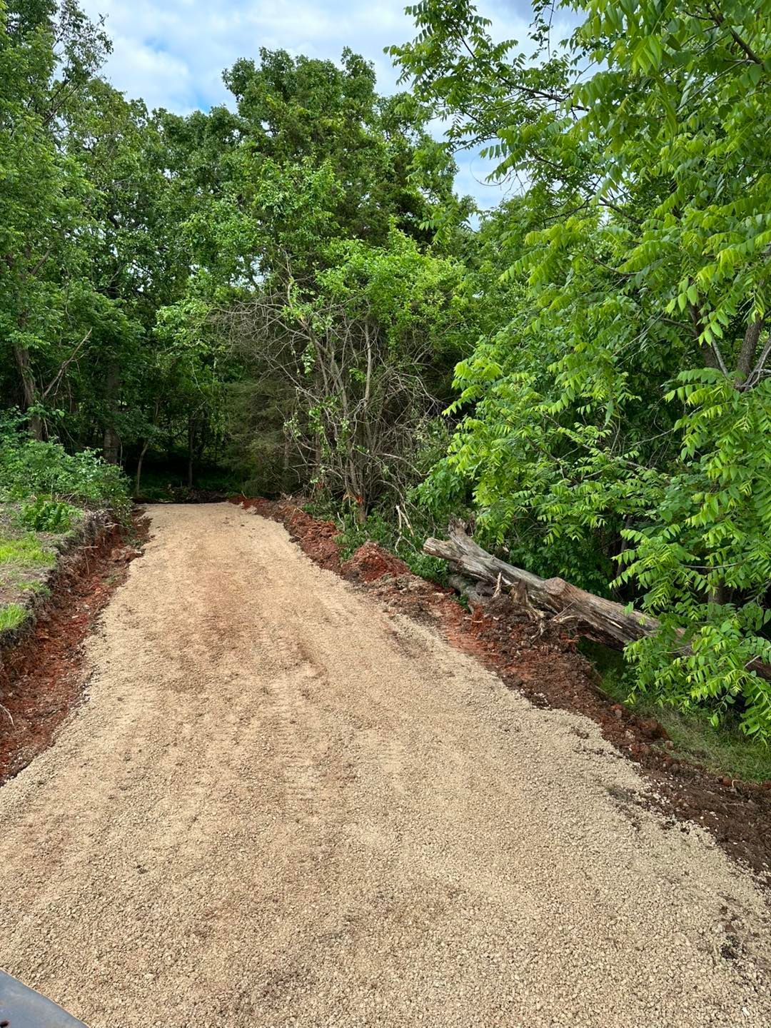 Fresh gravel path curving through lush green trees and brush in a wooded area