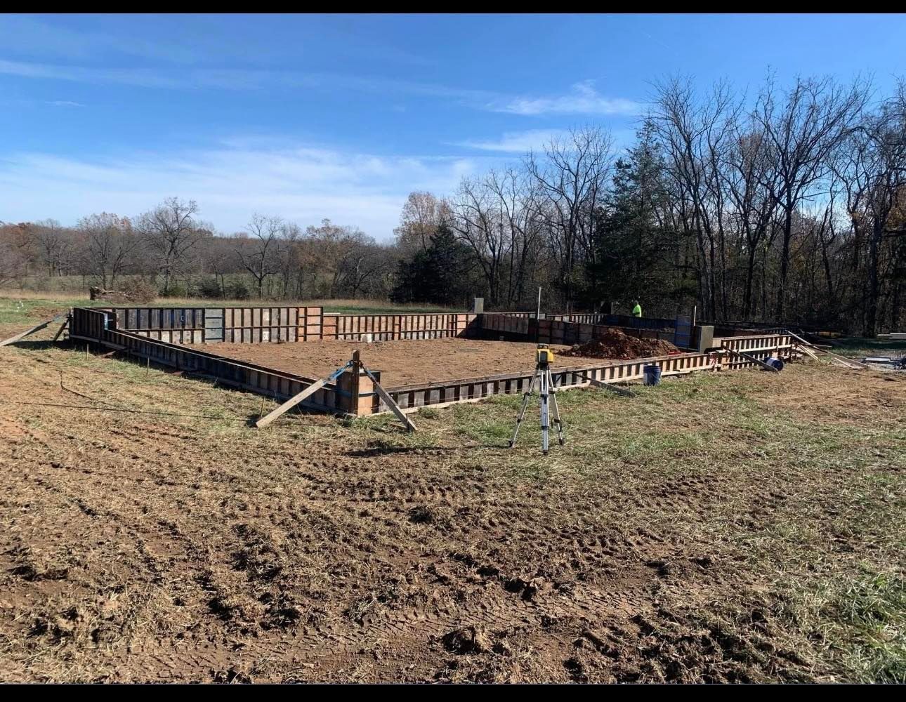 Construction site with wooden foundation framing on a dirt lot under a clear blue sky