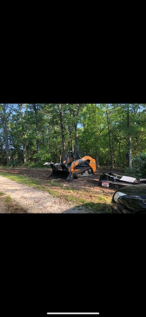 Orange excavator clearing debris in a wooded area beside a dirt path