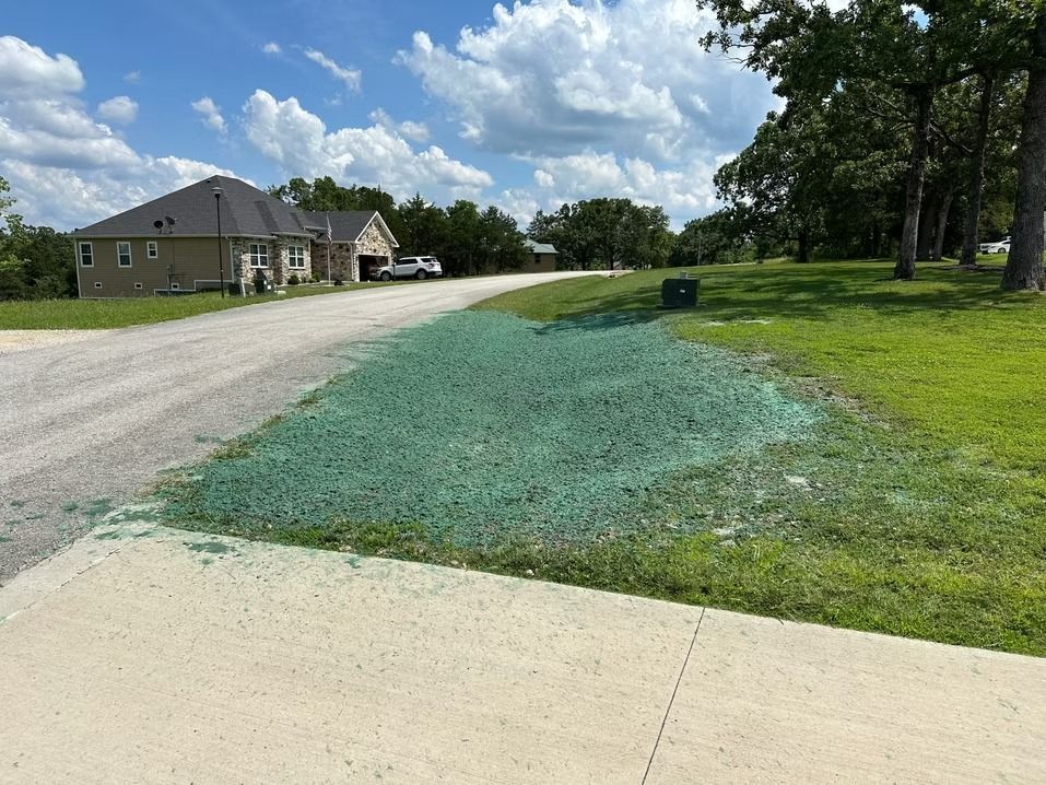 Gravel road beside a house and grassy yard under a cloudy blue sky