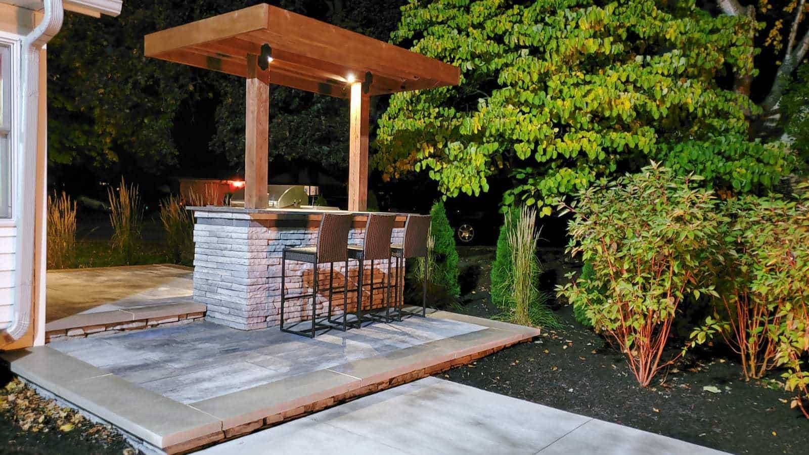 Outdoor bar with a brick base, wooden canopy, and seating, at night.