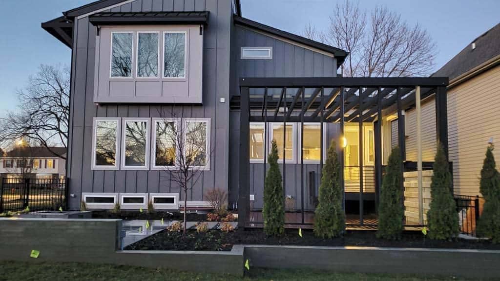 Modern gray house exterior with a pergola and small evergreens.