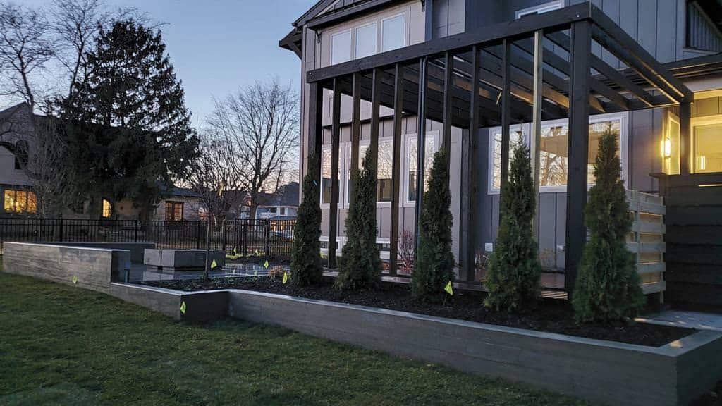 Modern house exterior at dusk with large glass windows, lit interior, and landscaped stone planter beds.